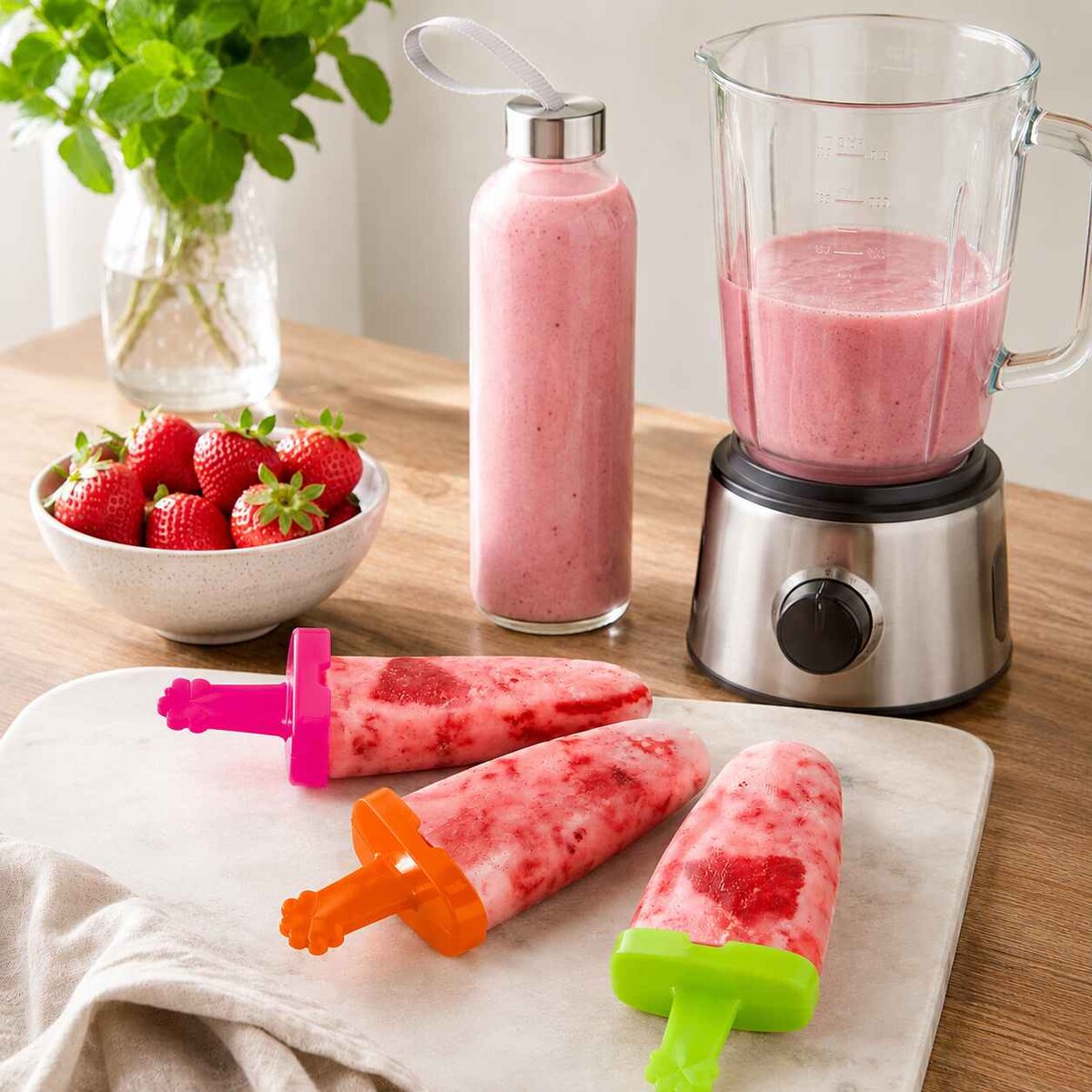 jahodové nanuky ve formách na nanuky a skleněná láhev s jahodovým smoothie